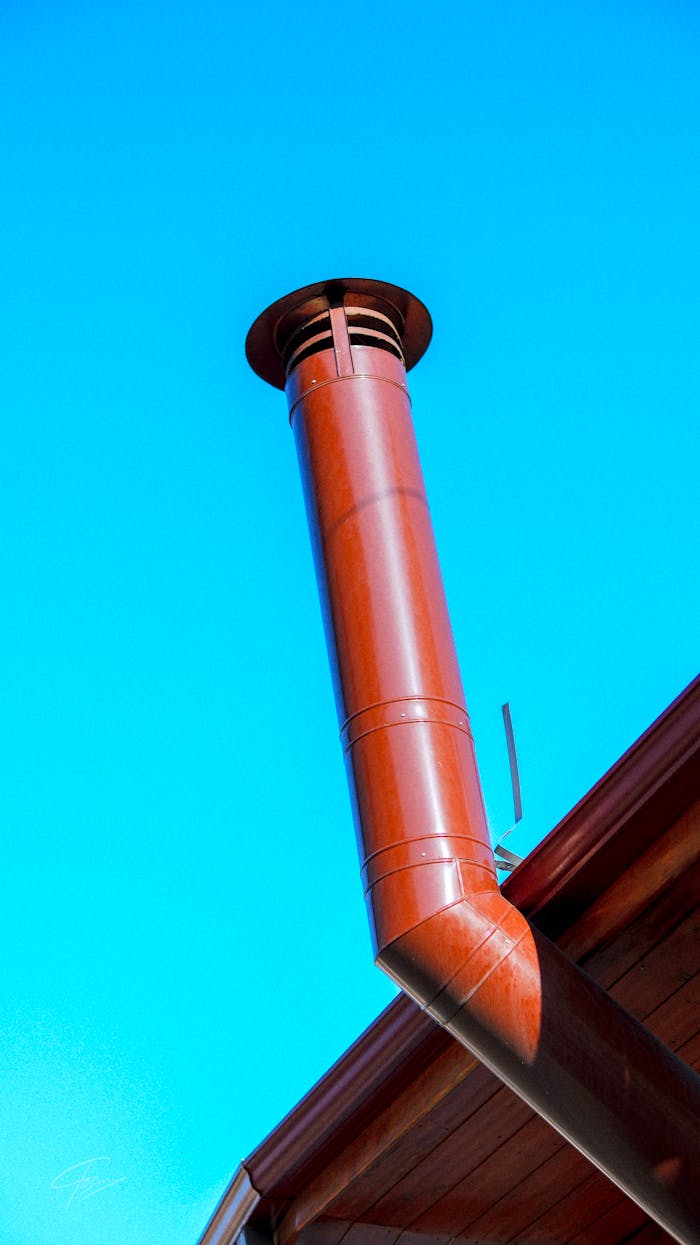 Close-up of a red chimney on a roof against a clear blue sky.