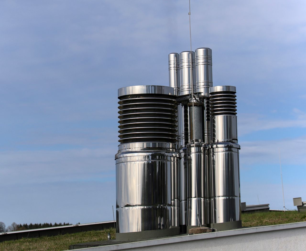 Reflective steel chimneys on a rooftop, contrasting with a clear blue sky, symbolizing modern industry.