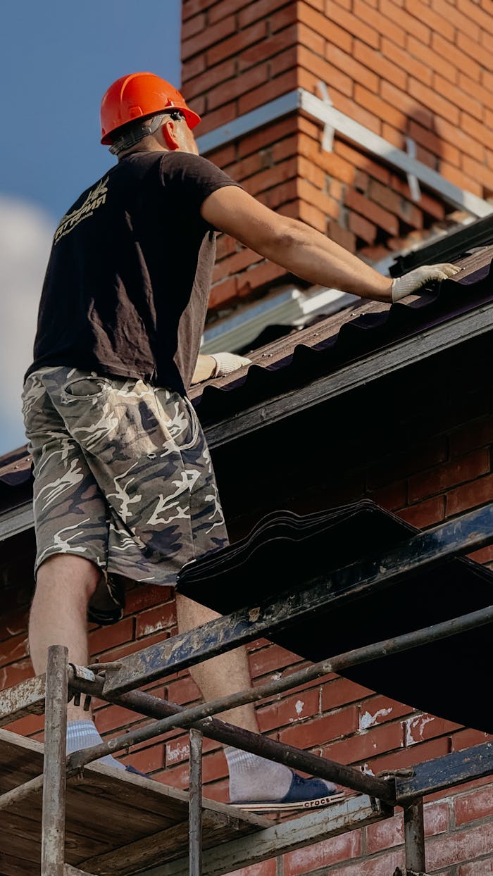 A construction worker wearing a hard hat works on a residential roof repair.